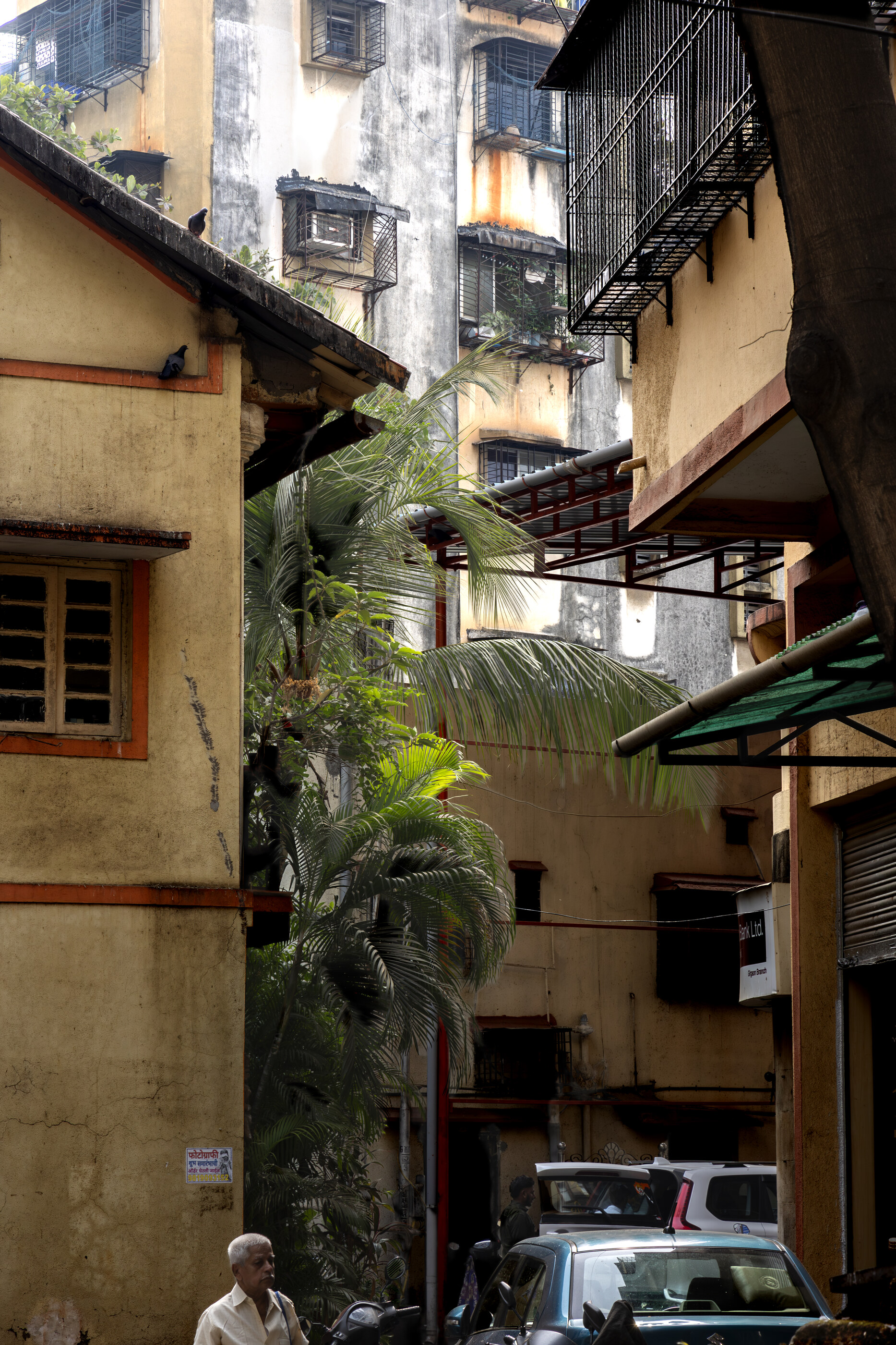An Indian street with old timber-balconied buildings and a parked vehicle, dense urban India. No single dominant person. Travel-as-subject through architecture and street life.