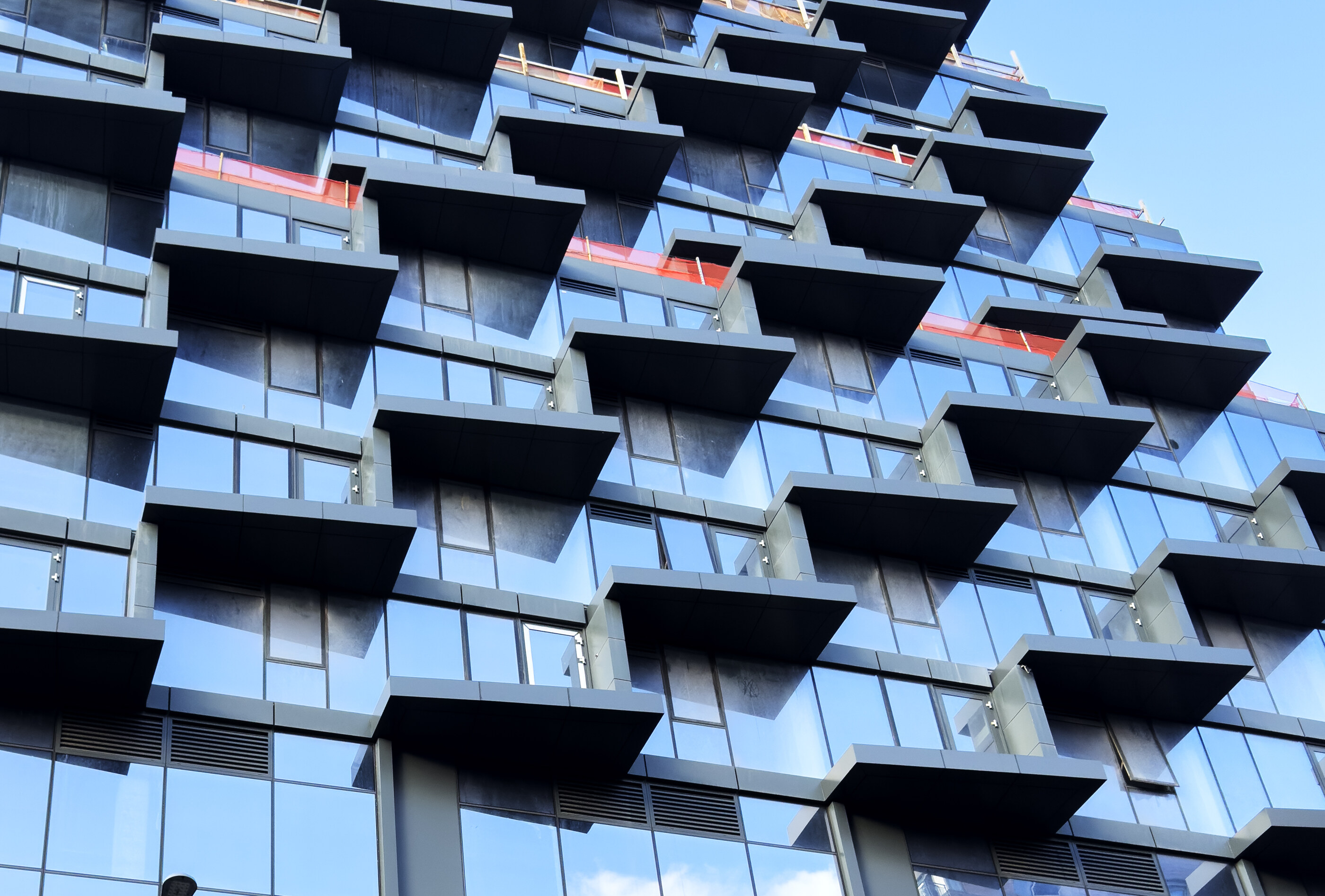A close detail of a modern building with deep blue-tinted glass and stacked angular balconies. The repeating geometric pattern fills the frame. No people. Built form as graphic.