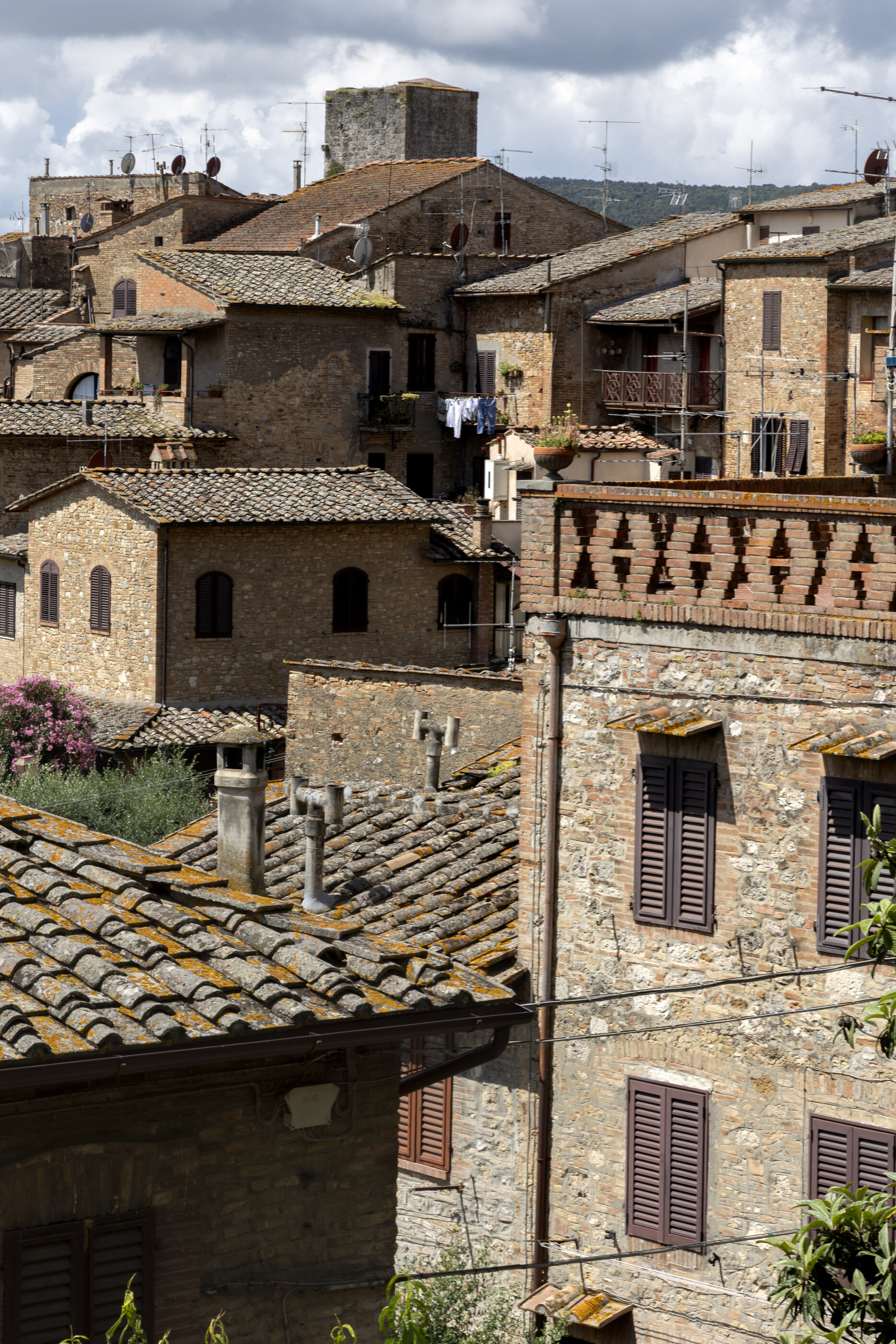 Closely packed terracotta and stone rooftops of an Italian hill town from above. No people. The architectural massing of the village is the subject — built form.