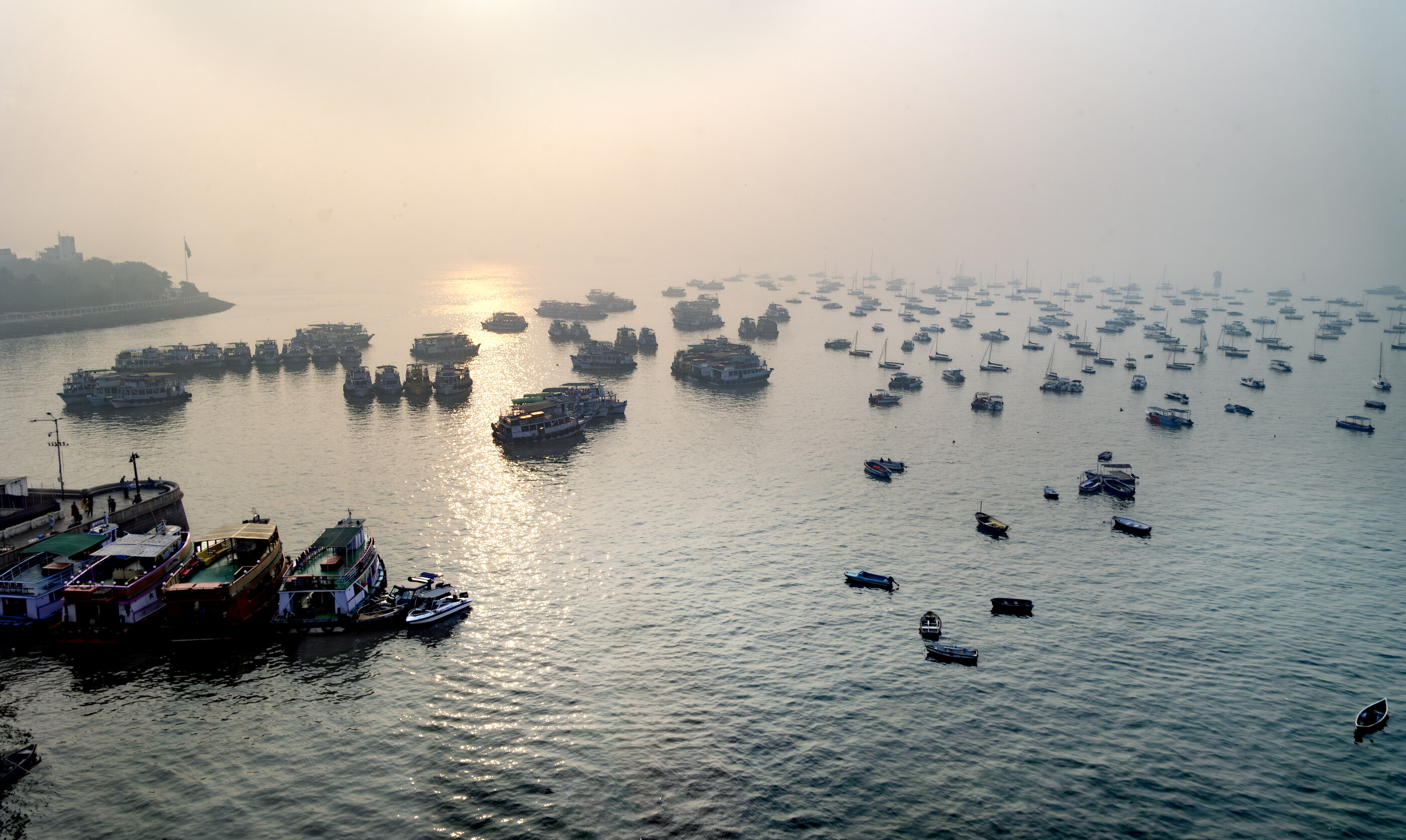 A wide bay at sunset filled with many small moored boats, distant hills behind. No dominant person. The composed bay full of boats is a place photograph with travel undertones.