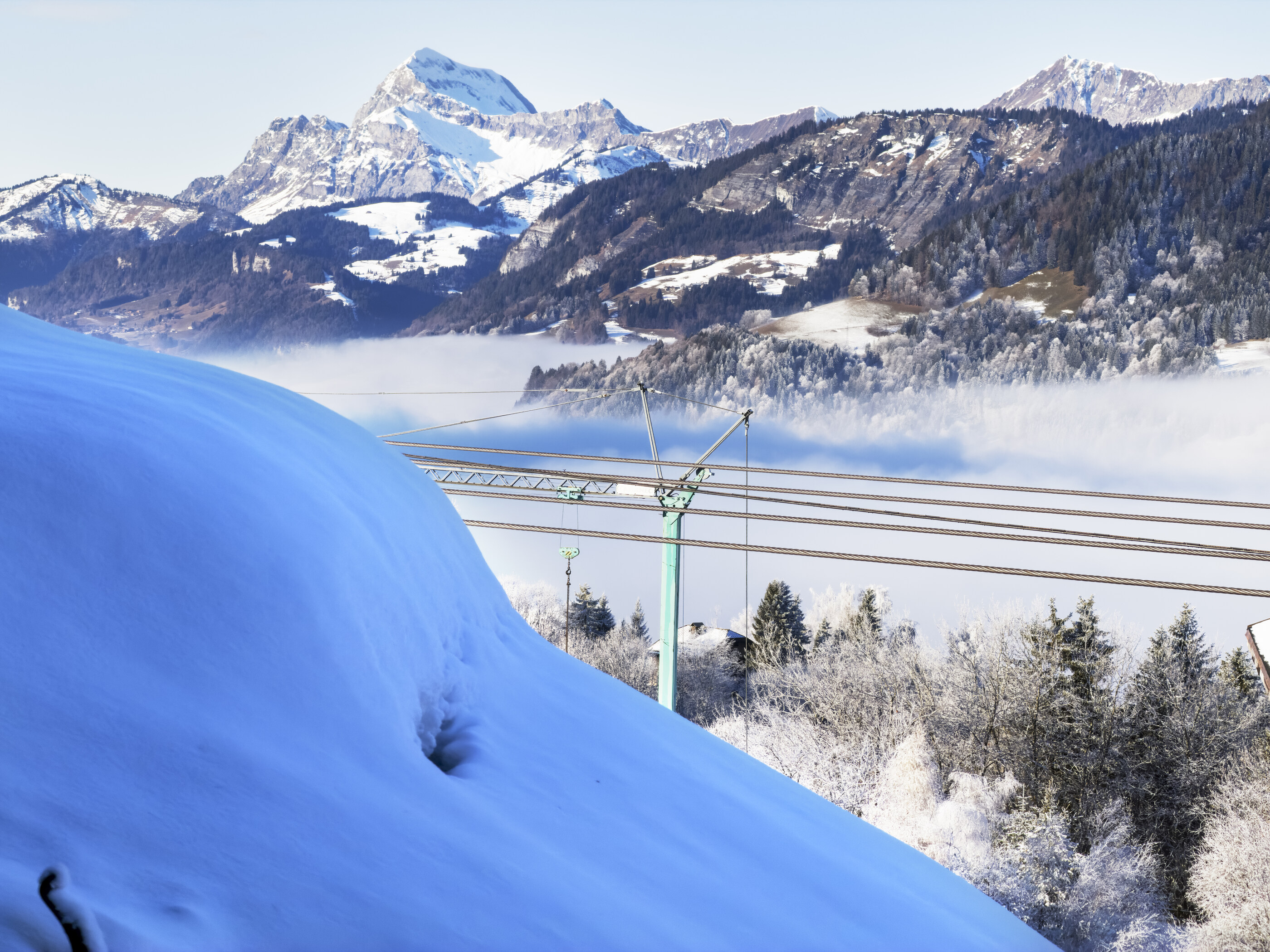 Ski-lift cables and pylons crossing a snowy mountain slope with mist below.