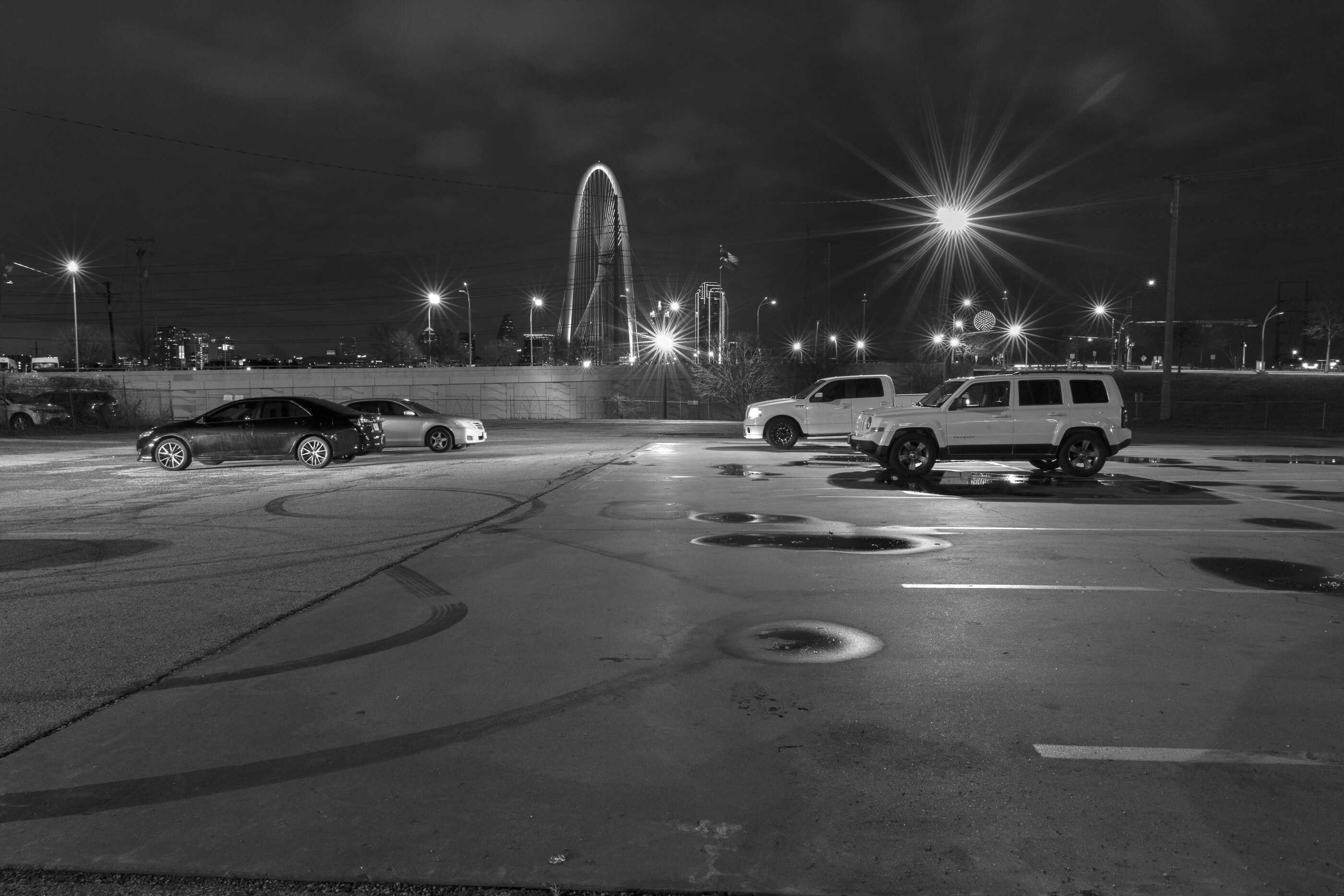 A black-and-white long-exposure of cars on a road at night, headlight trails streaking across the frame.