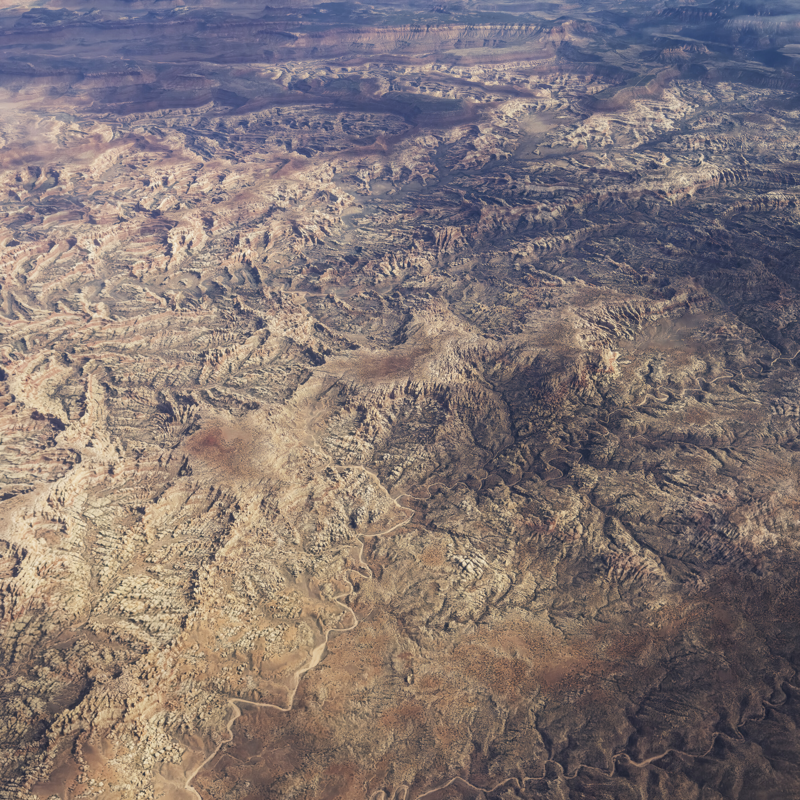 An aerial topographic view of a desert/canyon landscape, abstract patterns of erosion in browns and greys.