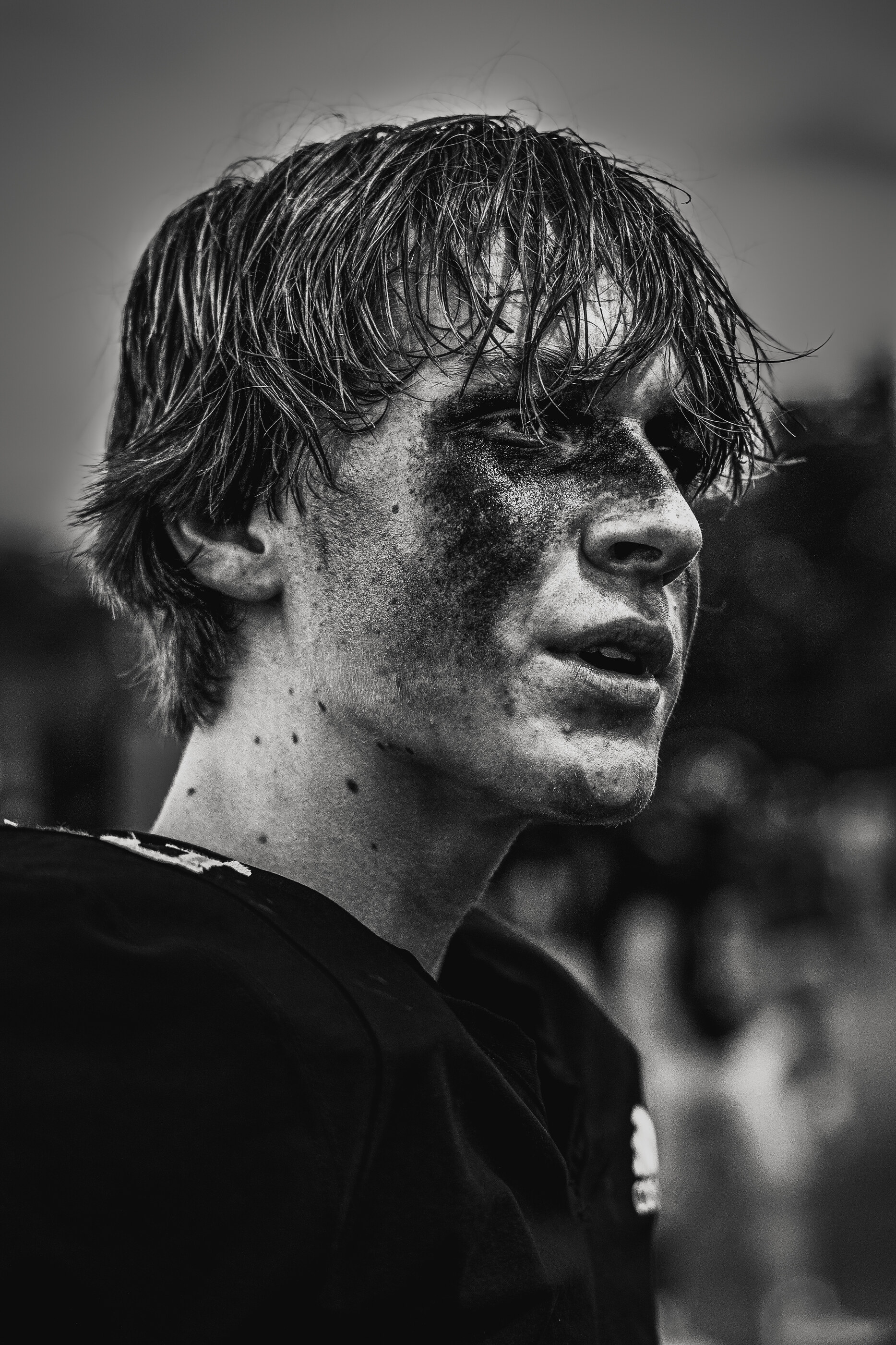 A black-and-white close-up portrait of a young man with messy hair, intense look at camera. He fills the frame. Single dominant human subject.