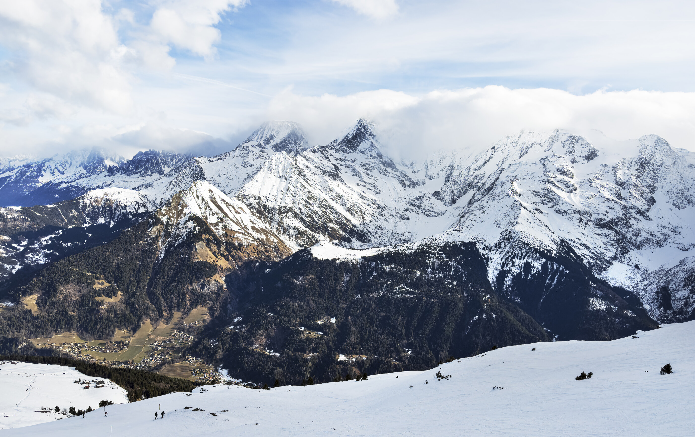 A wide alpine landscape with snowy peaks and a foreground meadow, no athletic activity and no skiers visible. The land at scale is the subject. Pure place.