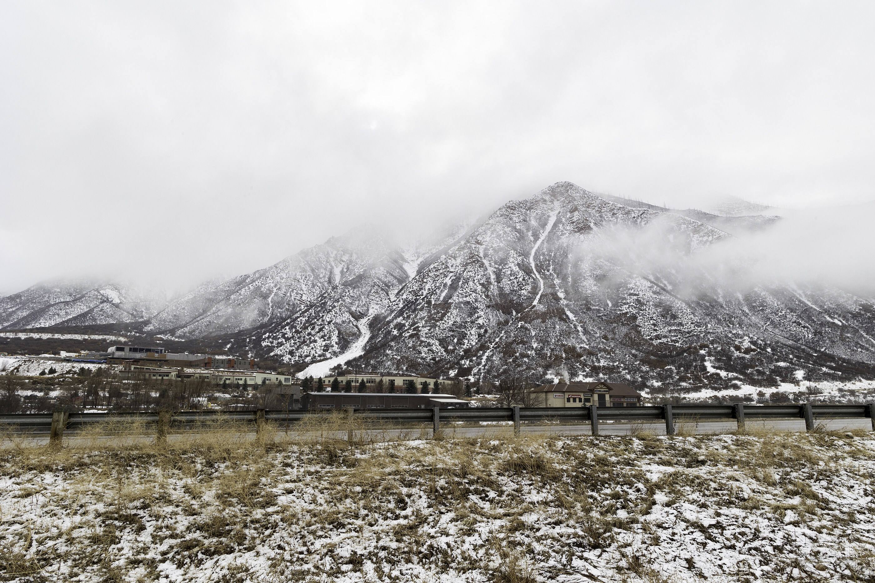 A black-and-white wide view of a snowy mountain looming over a flat valley. No people. The mountain at scale is the subject.