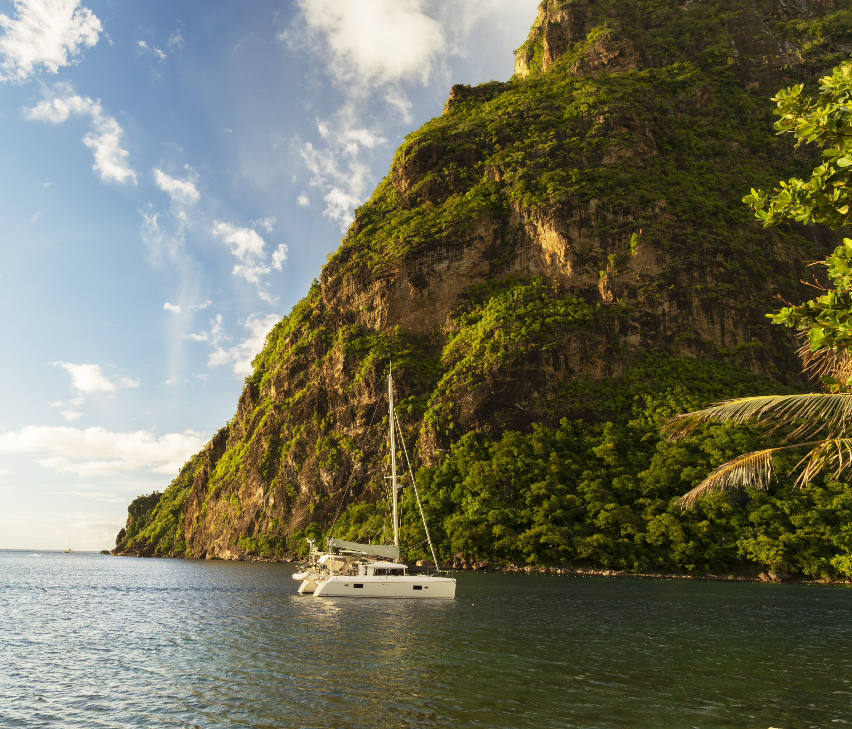 A steep coastal cliff dropping to water with a small boat moored below. The cliff and water dominate; the boat is incidental scale-marker. Land at coastal scale is the subject.
