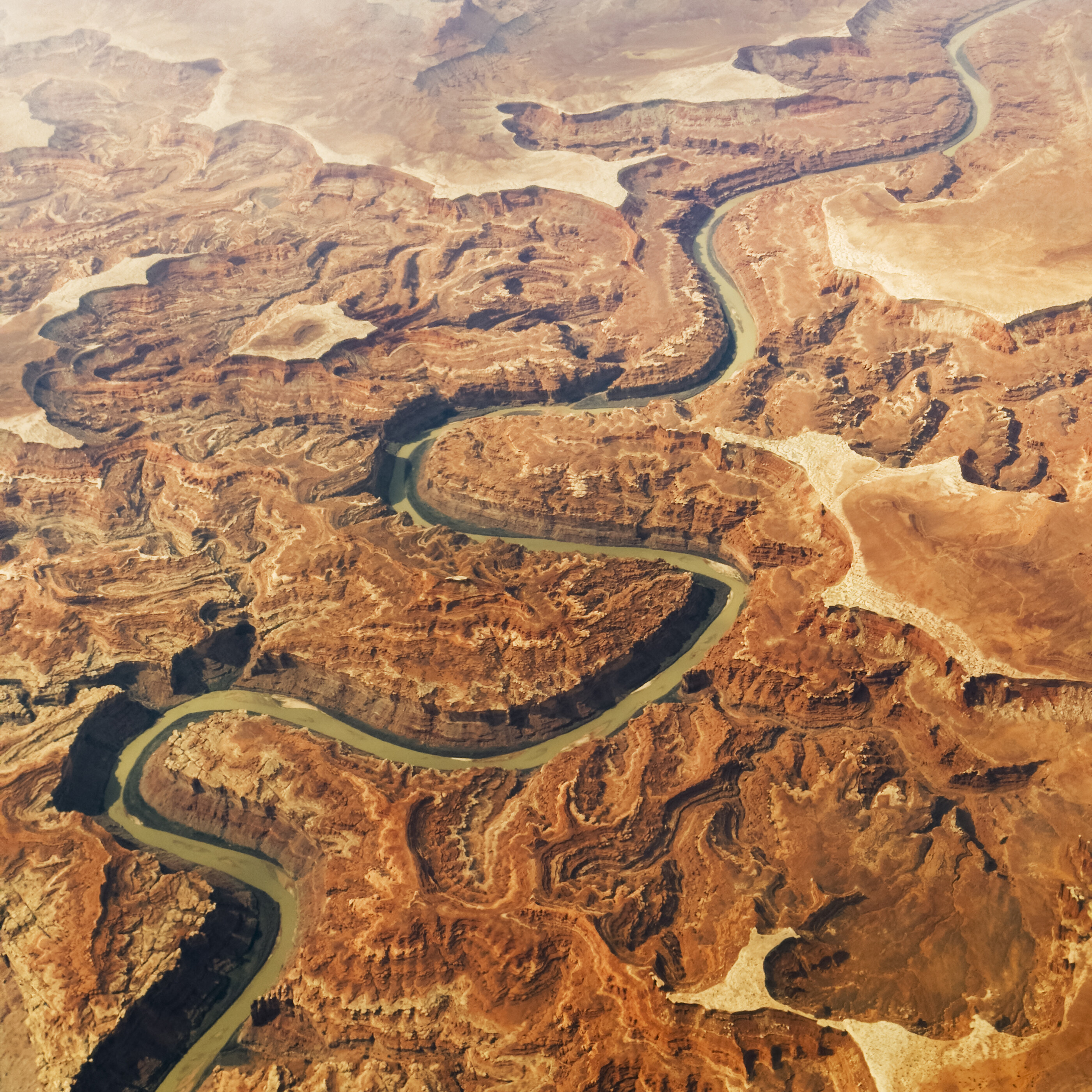 An aerial view of a winding river through red Utah/canyon country, abstract patterns of erosion. No people. The land from above as graphic and place.