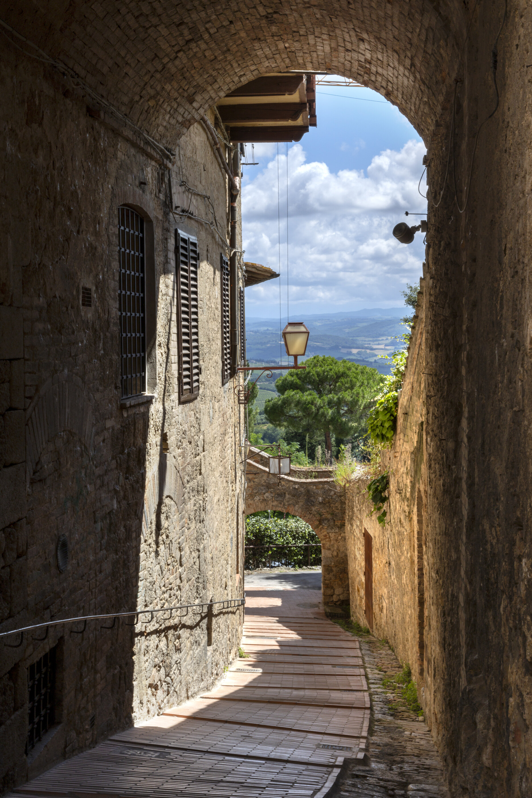 A narrow stone passage / temple archway with steps descending toward an opening, a figure visible at the far end. The architecture is religious / templed; passage to a sacred space is the subject.