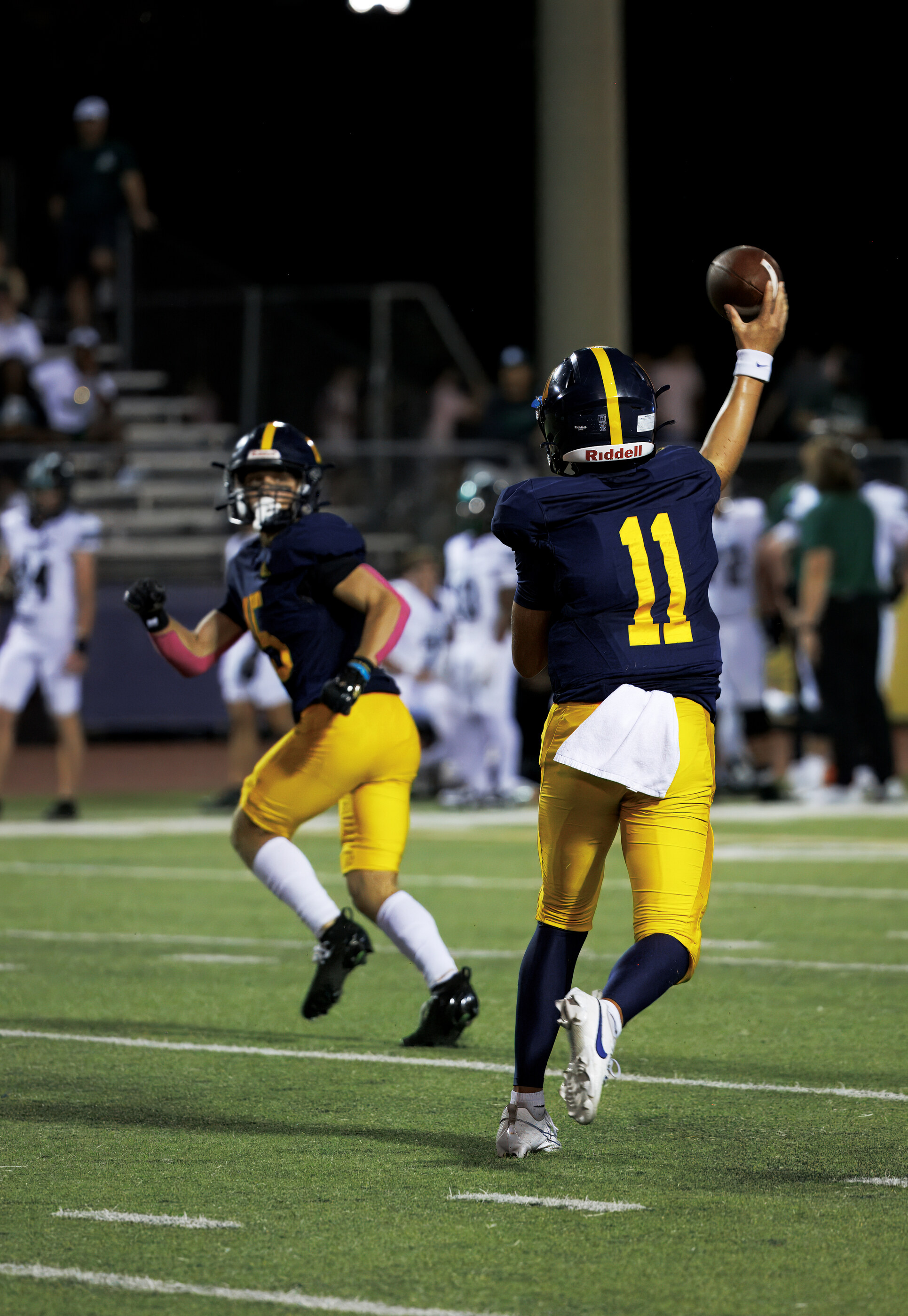 A quarterback in full throwing motion under stadium lights, ball just released. Athletic action is the subject.