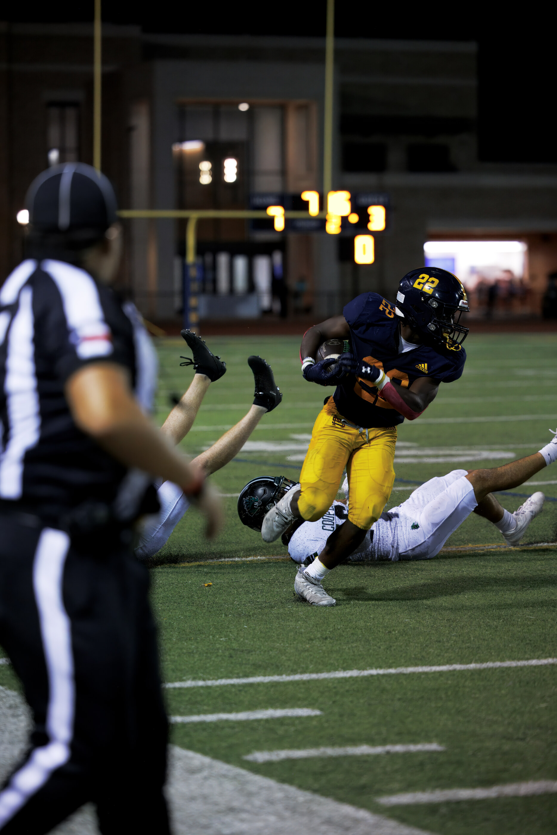 A football game action shot, two players colliding in motion under stadium lights. Athletic activity dominates.