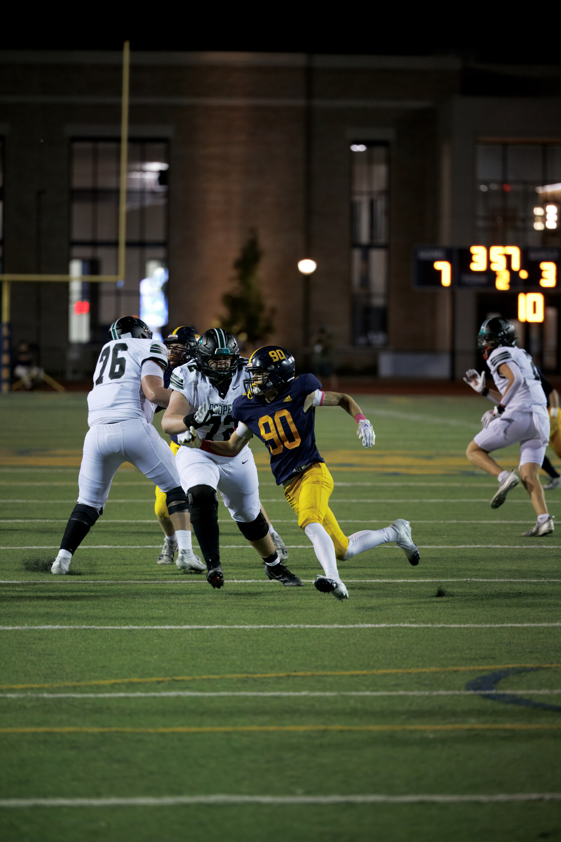 A football play in progress, several players in motion under bright field lights. Athletic action.