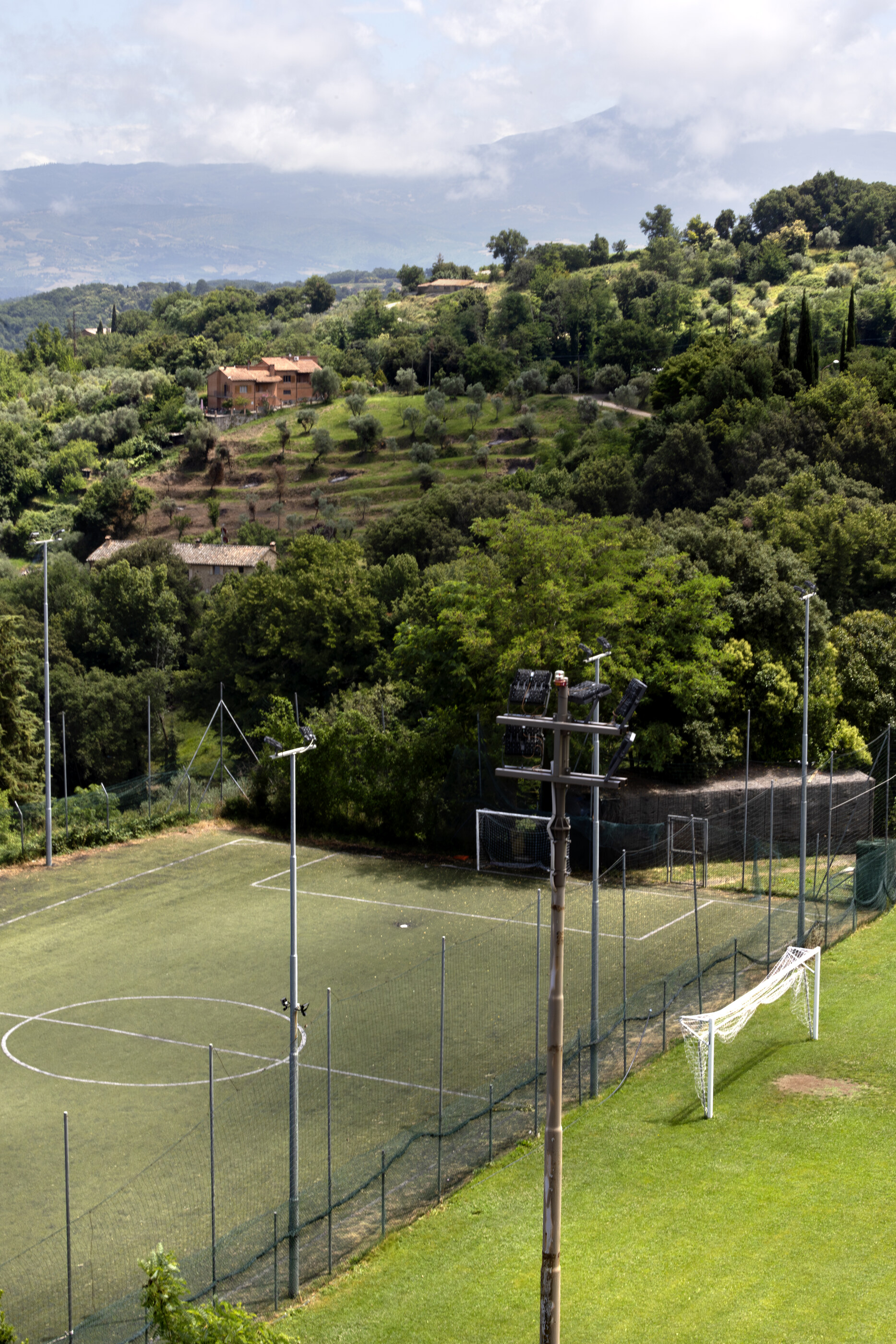 An empty green field bordered by a chain-link fence under daylight, looking like an unused soccer pitch.