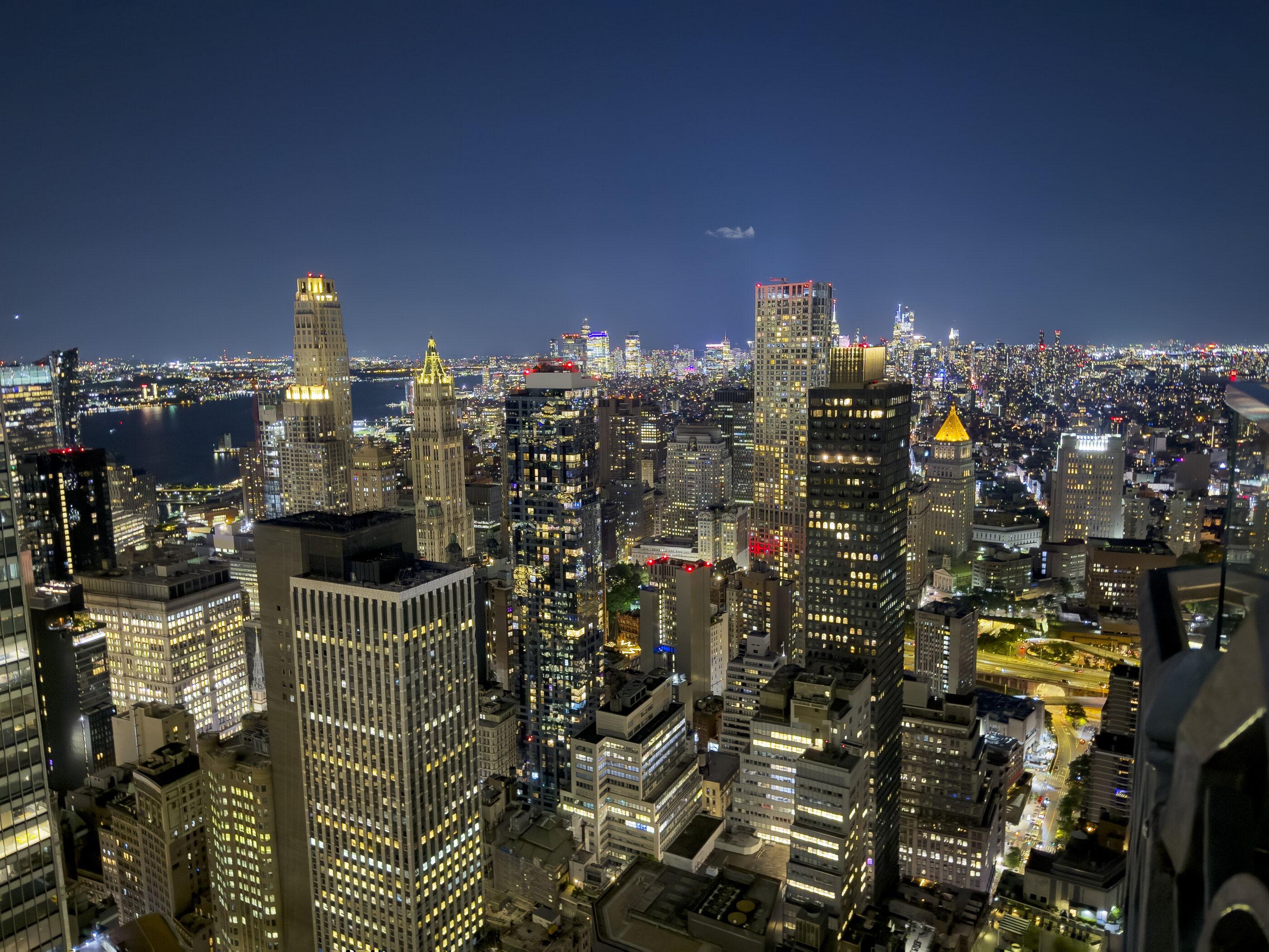 A night cityscape from above — dense towers, lit windows, the lattice of a skyscraper city at full glow. No visible human. The city itself as scene is the subject.