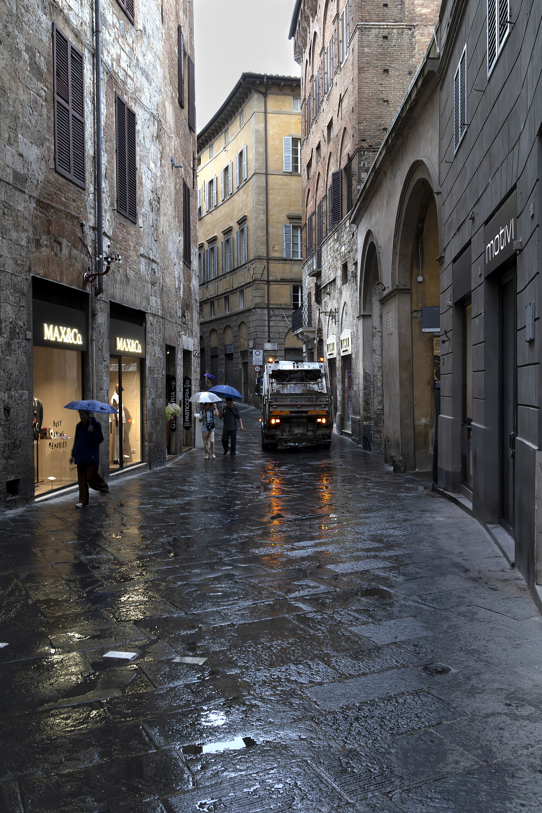 A wet European cobblestone street after rain, narrow, lined with old buildings.